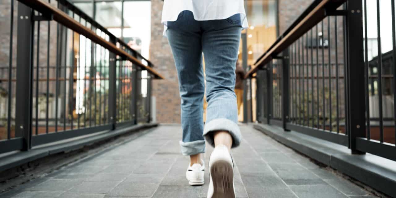Back view of a woman in jeans and sneakers walking in the street
