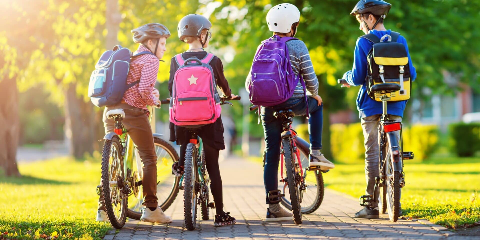 Children with rucksacks riding on bikes in the park near school