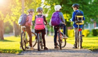 Children with rucksacks riding on bikes in the park near school