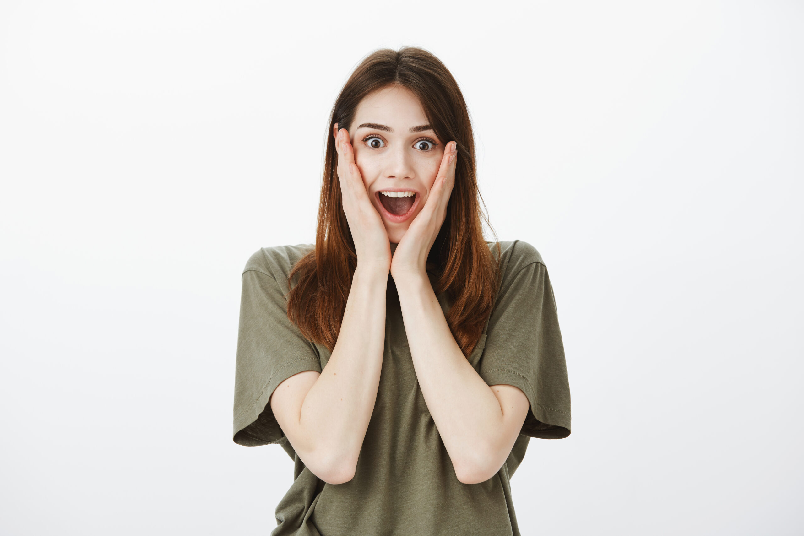 Excited cute girlfriend screaming from positive surprise, amazed. Studio shot of overwhelmed wondered european woman, holding palms on cheeks and smiling from satisfaction receiving unbelievable gift