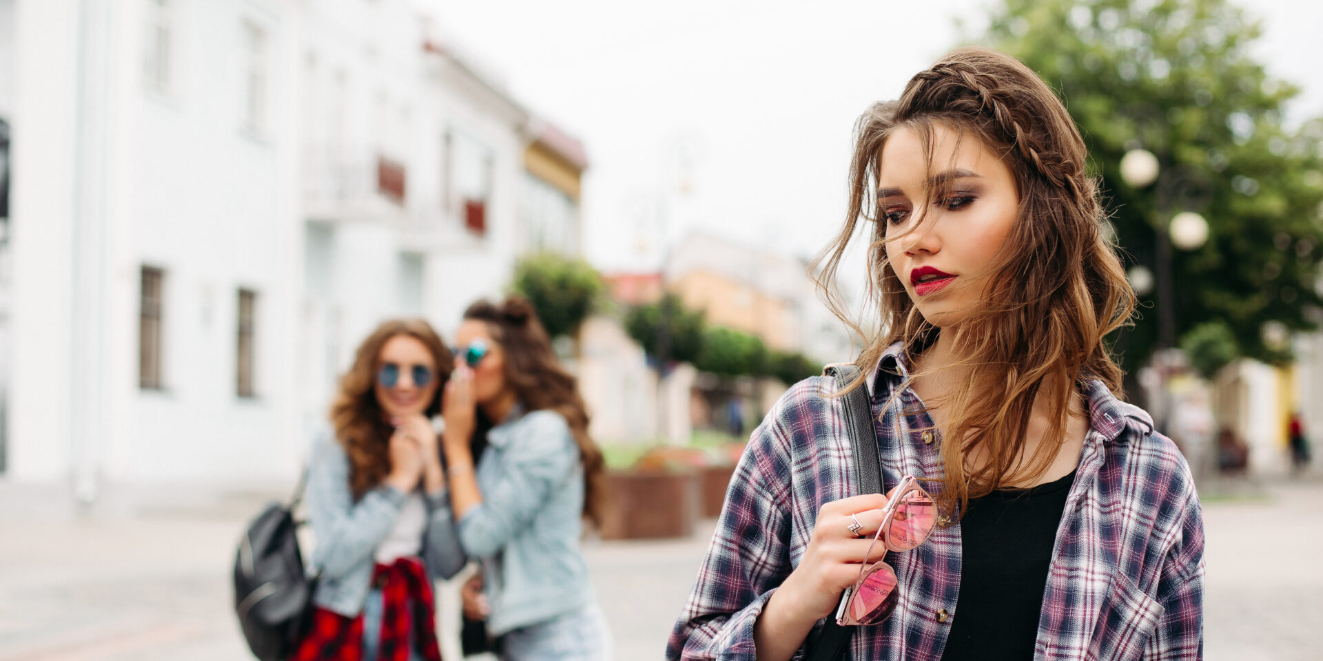 Jealous girls whispering about third girl in front of camera.