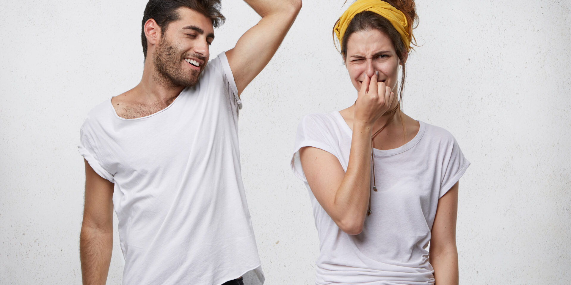 Bad smell and body odor. Picture of fastidious young woman pinching her nose disgusted with terrible sweat, coming out from bearded man’s armpit who is standing next to her, raising his arm