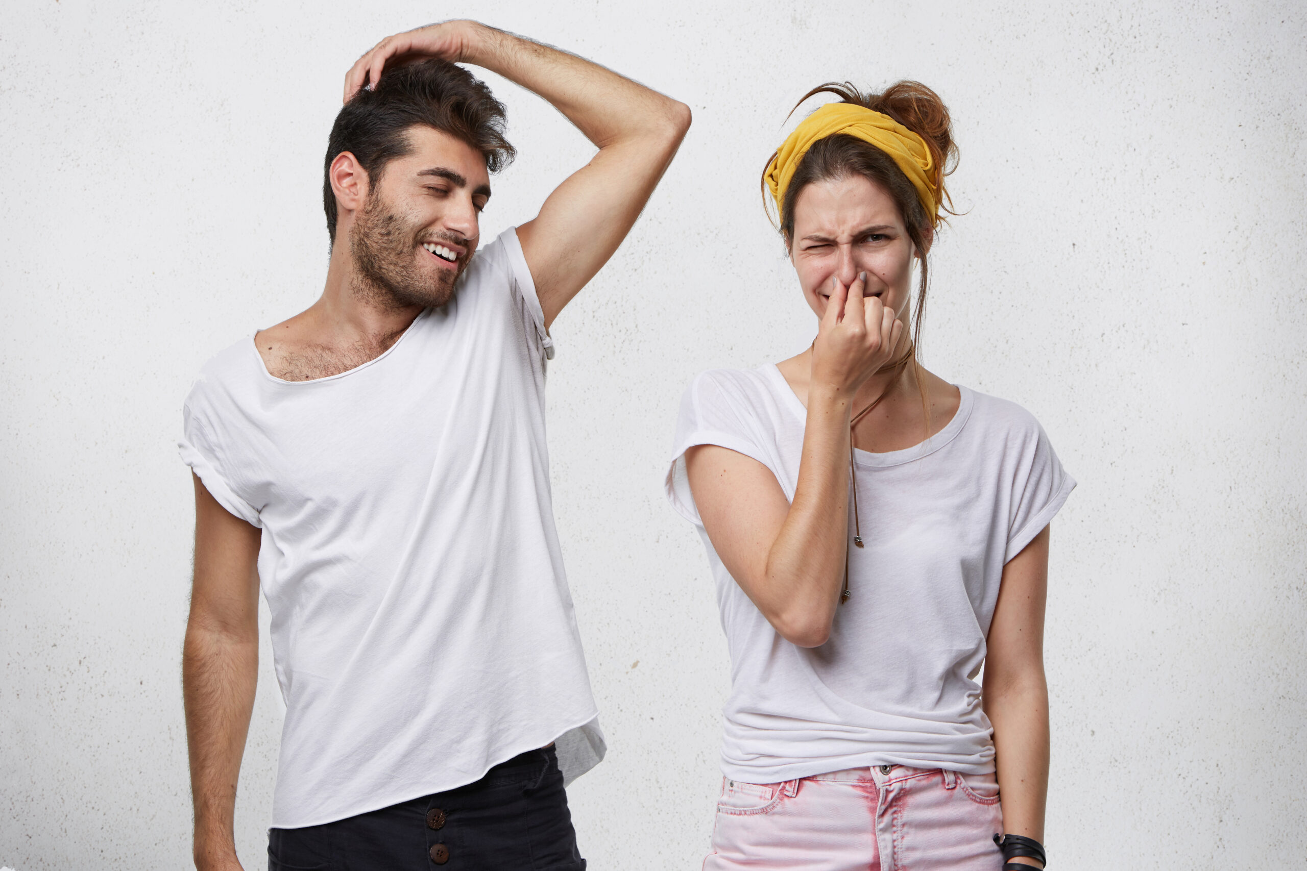 Bad smell and body odor. Picture of fastidious young woman pinching her nose disgusted with terrible sweat, coming out from bearded man’s armpit who is standing next to her, raising his arm