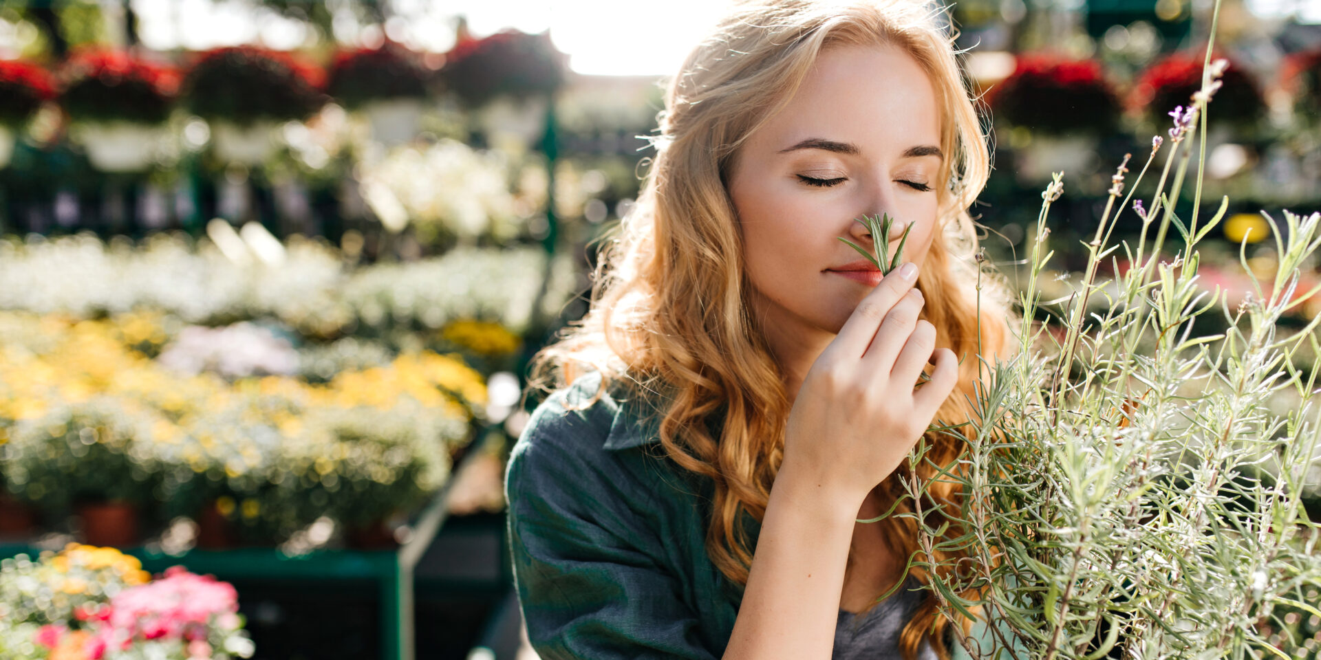 close-up portrait of plant lover admiring smell of lavender. Model in dark cotton clothes posing in botanical garden.