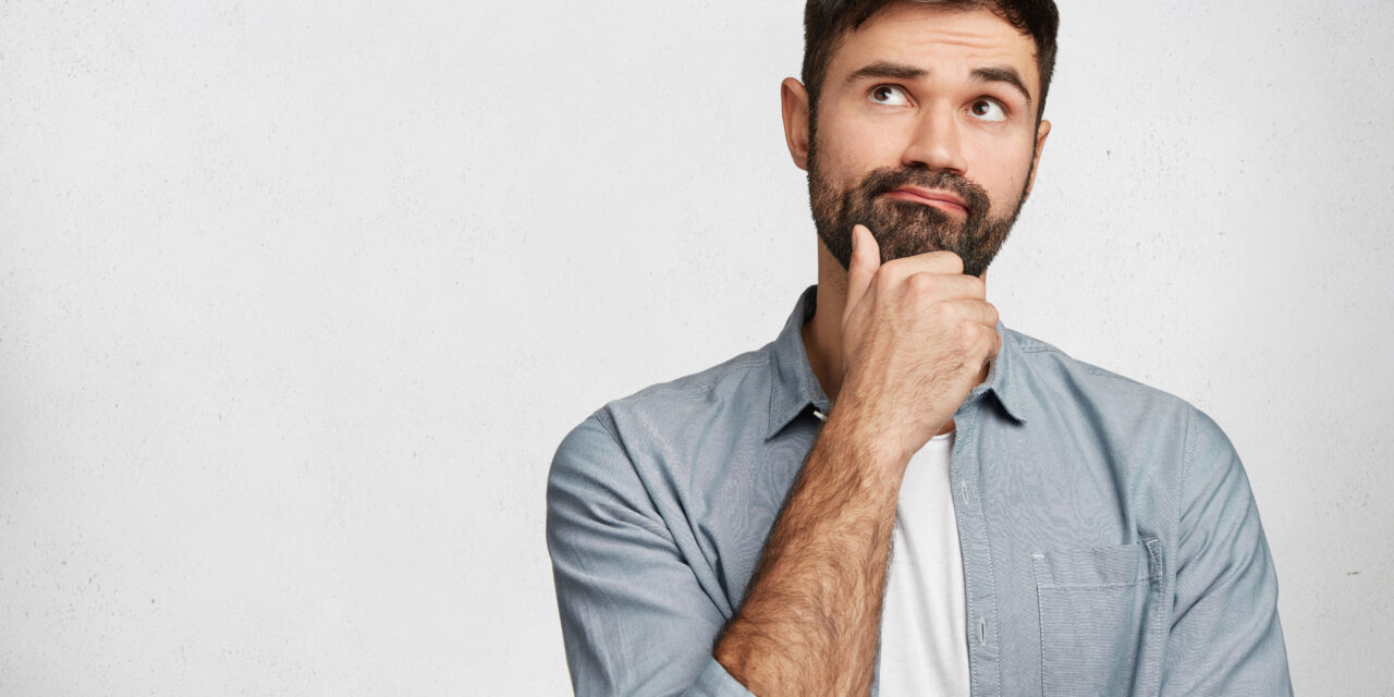 Thoughtful man with stubble looks pensively upwards, has pleasant dreams as plans his coming holidays, generates new ideas, isolated over white background with copy space for your advertising content
