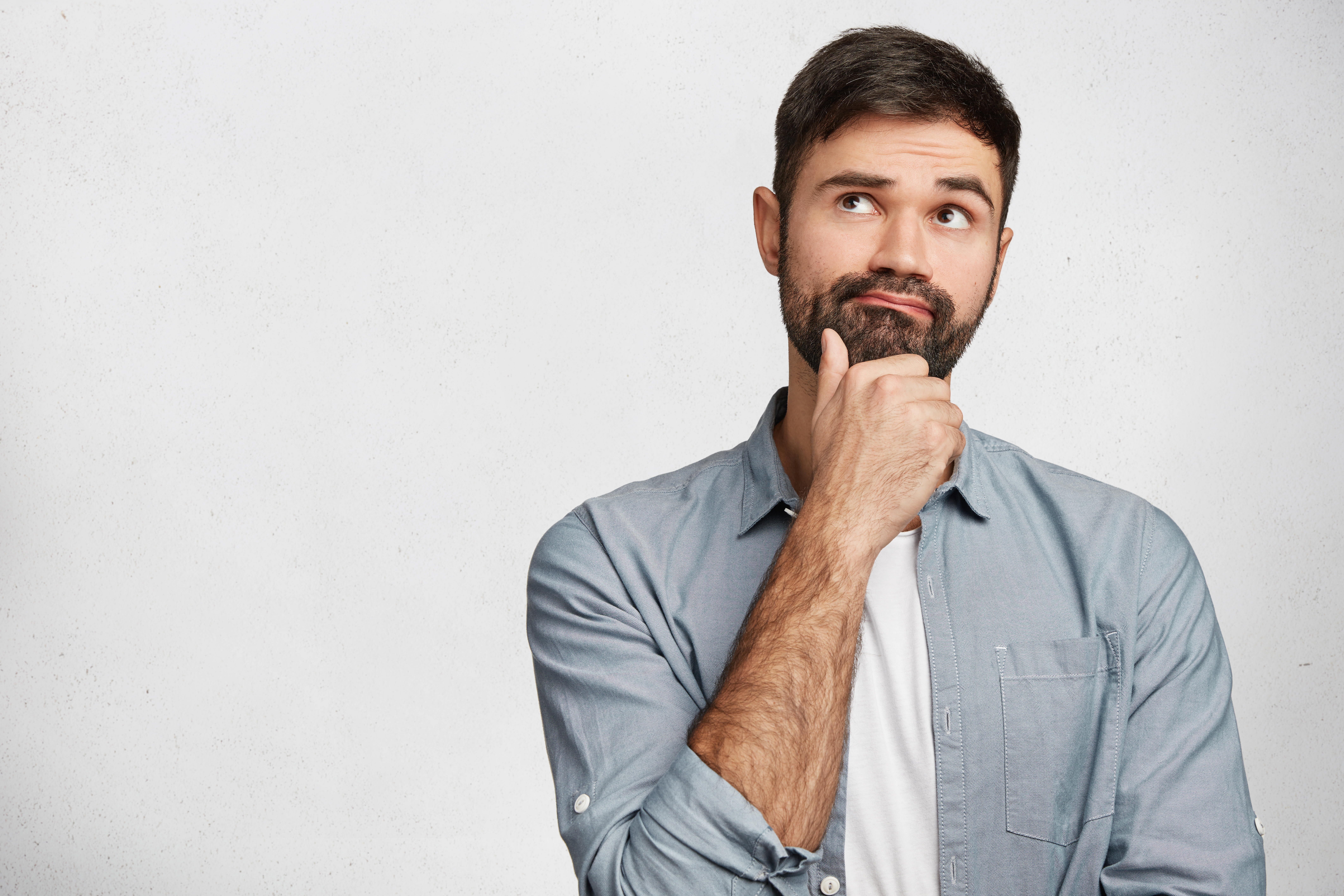 Thoughtful man with stubble looks pensively upwards, has pleasant dreams as plans his coming holidays, generates new ideas, isolated over white background with copy space for your advertising content