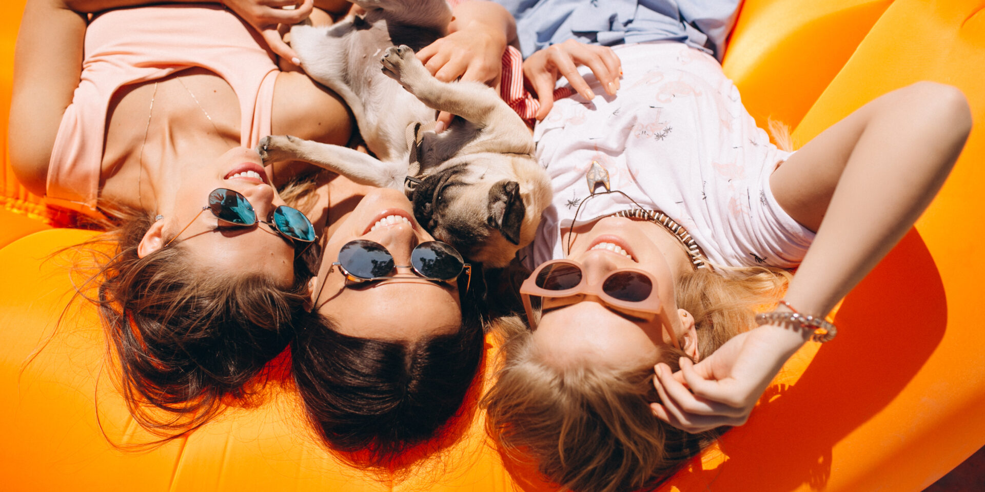 Three girls with small dog lying on pool mattress at the beach