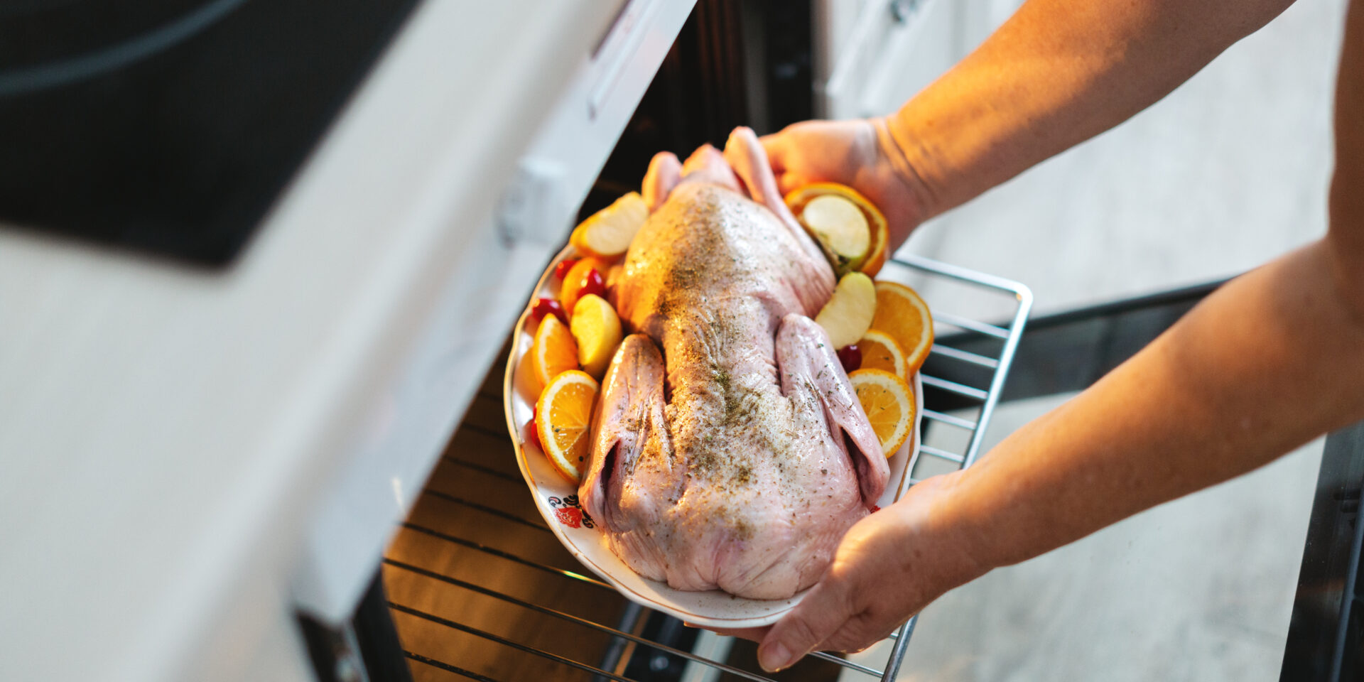 Woman puting raw duck with vegetables in oven