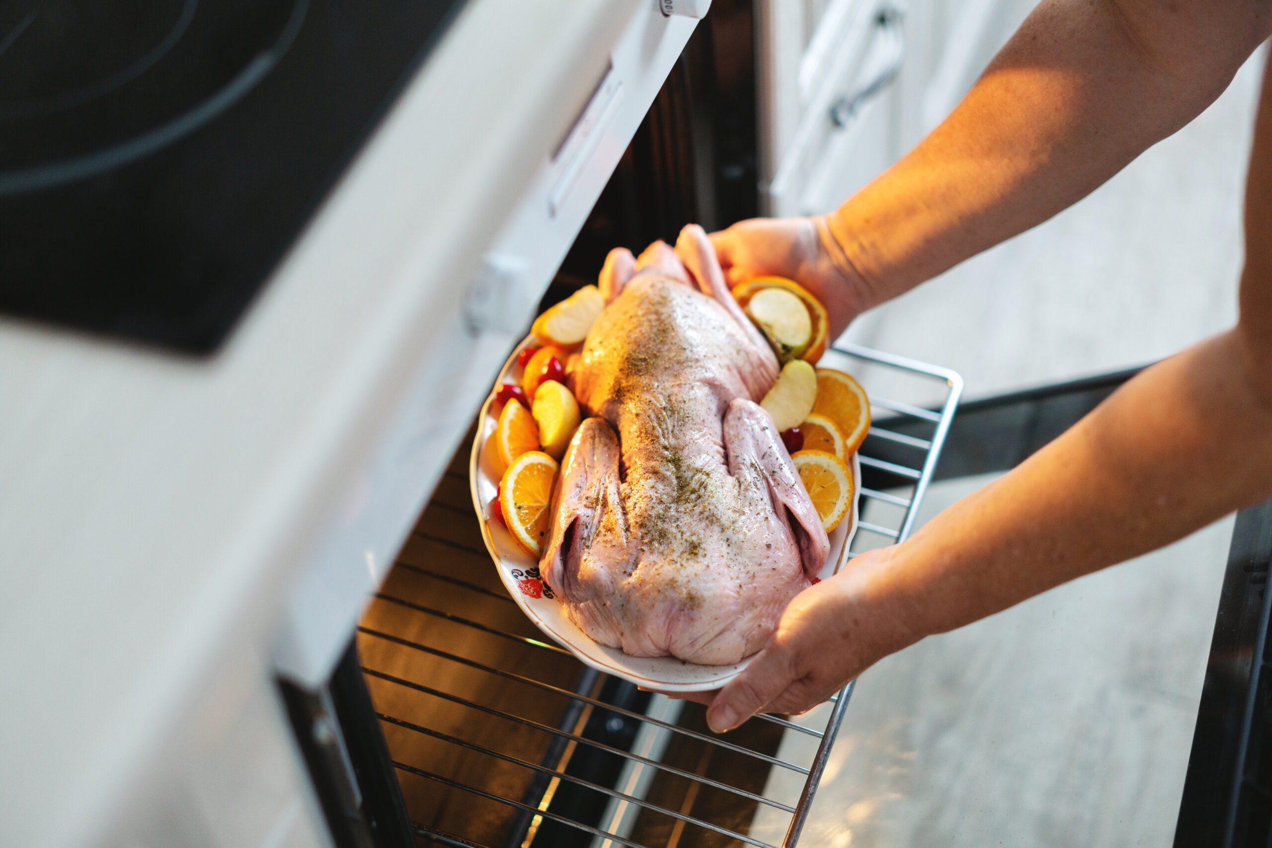 Woman puting raw duck with vegetables in oven