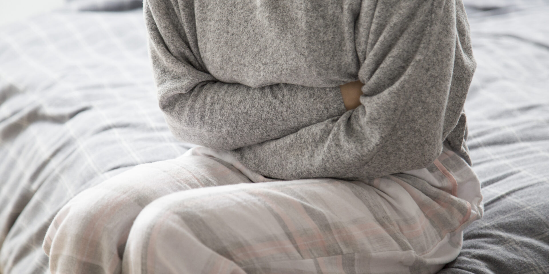 Sick woman on bed keeping hands on stomach, suffering from pain
