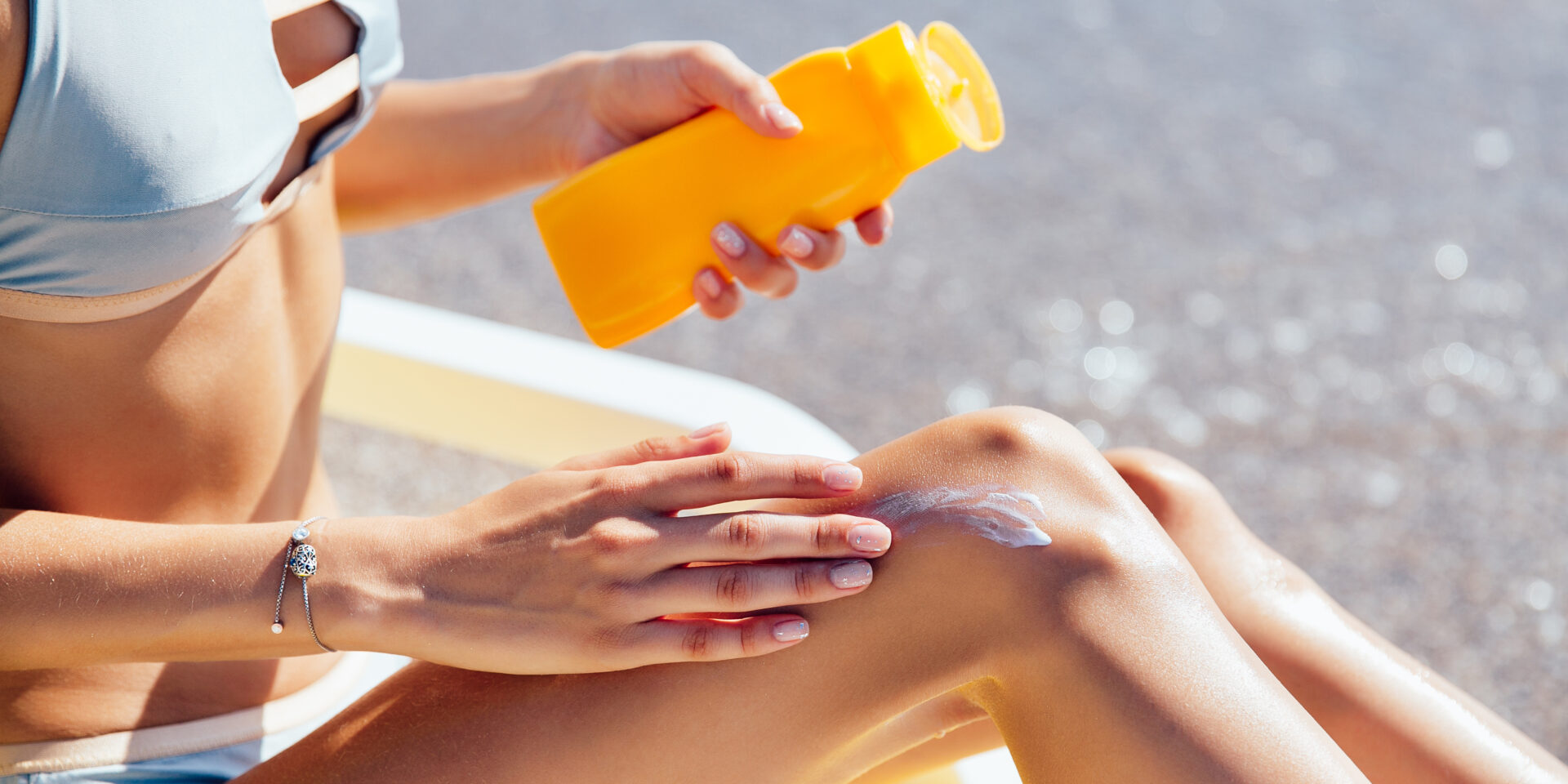 Woman in a swimsuit applying the cream on her legs, on the beach