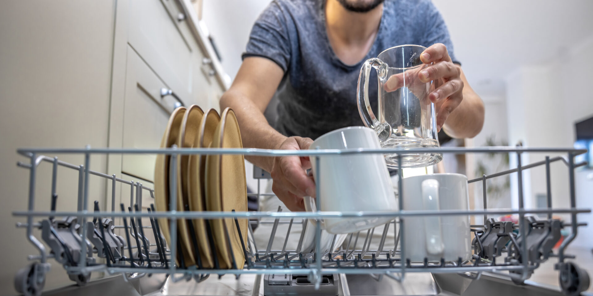 The man takes clean, washed dishes from the dishwasher.