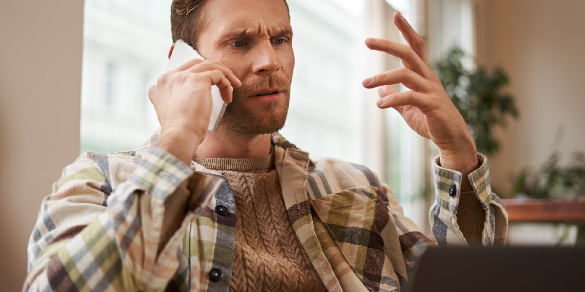 Portrait of confused man arguing with someone over the phone, businessman discuss project, looking at chart on laptop screen, using mobile phone to make a call, staring at monitor with frustration